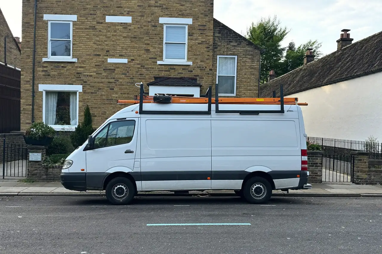 A plain white work van parked outside a British brick house